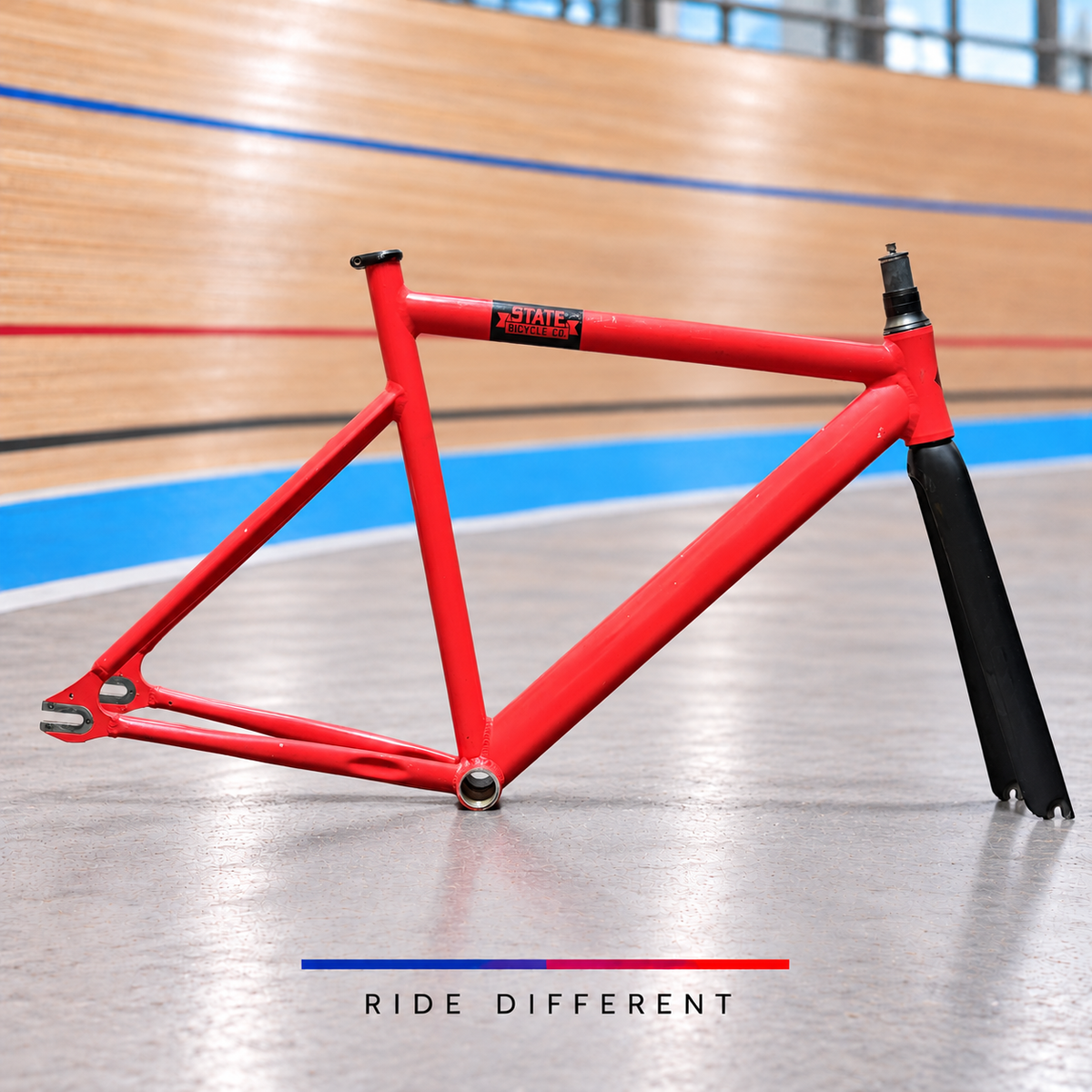 State red aluminium track frameset – side view with carbon fork on velodrome background